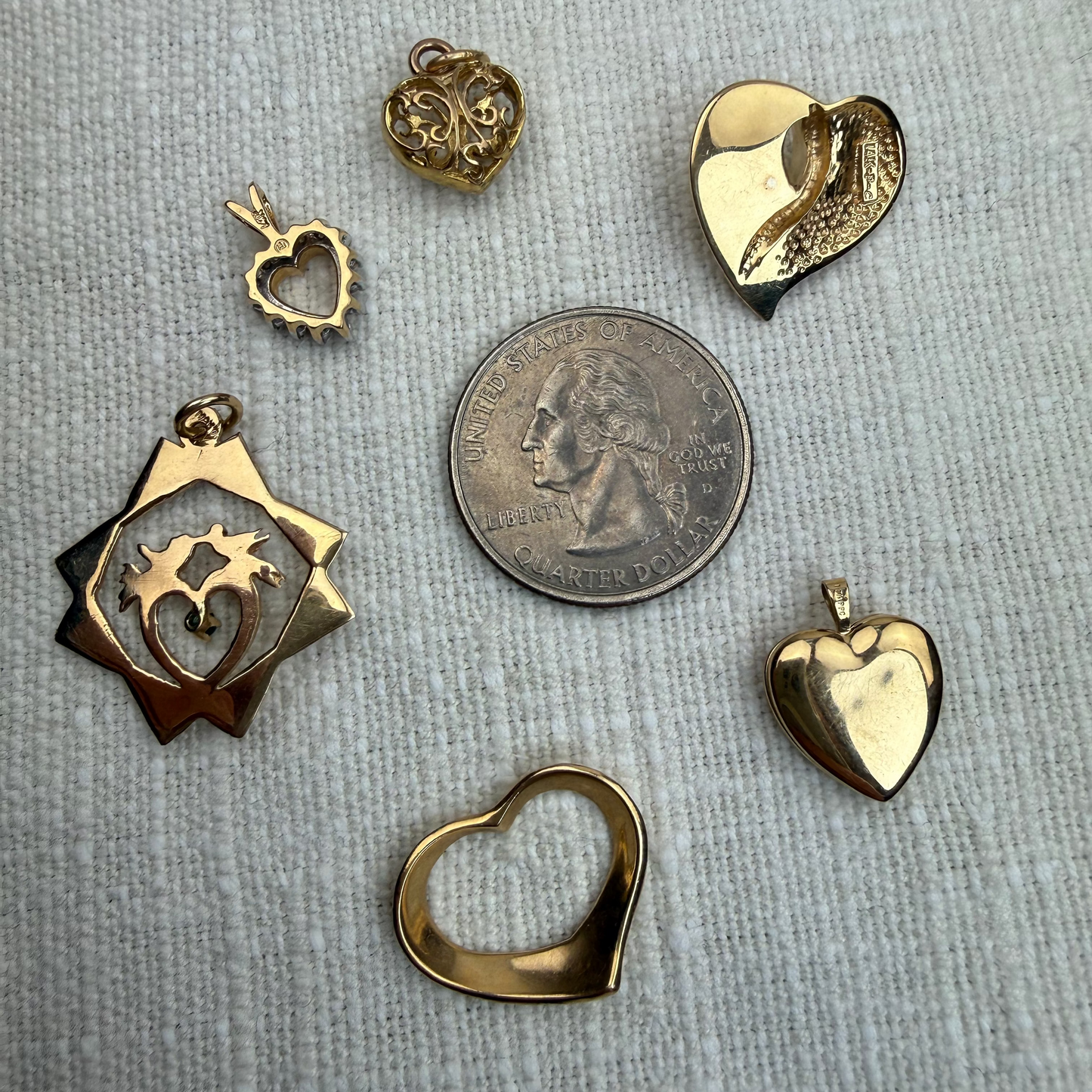 Gold heart-shaped pendants on a gray textured surface with a quarter for scale.
