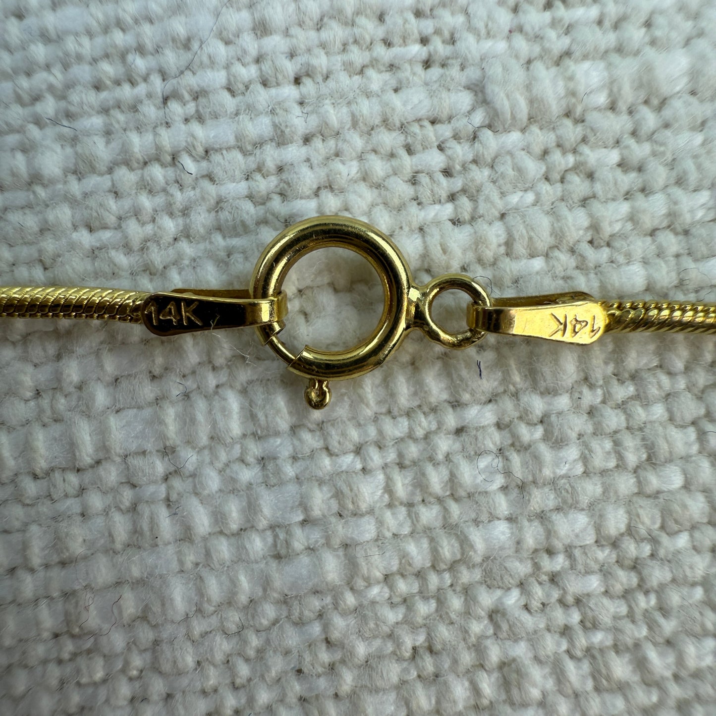 Gold bracelet with clasp on a textured beige surface