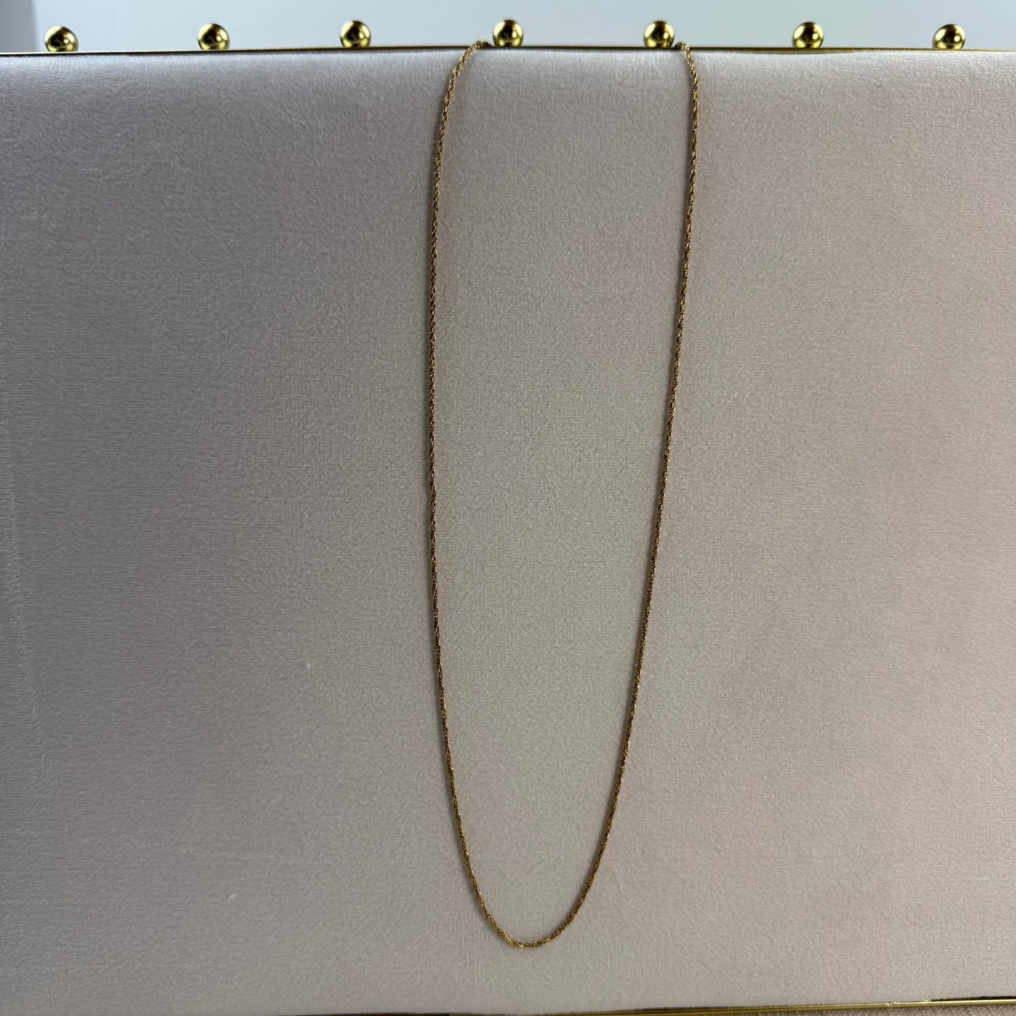 Gold chain draped over a light gray clutch bag with gold studs on a light blue background