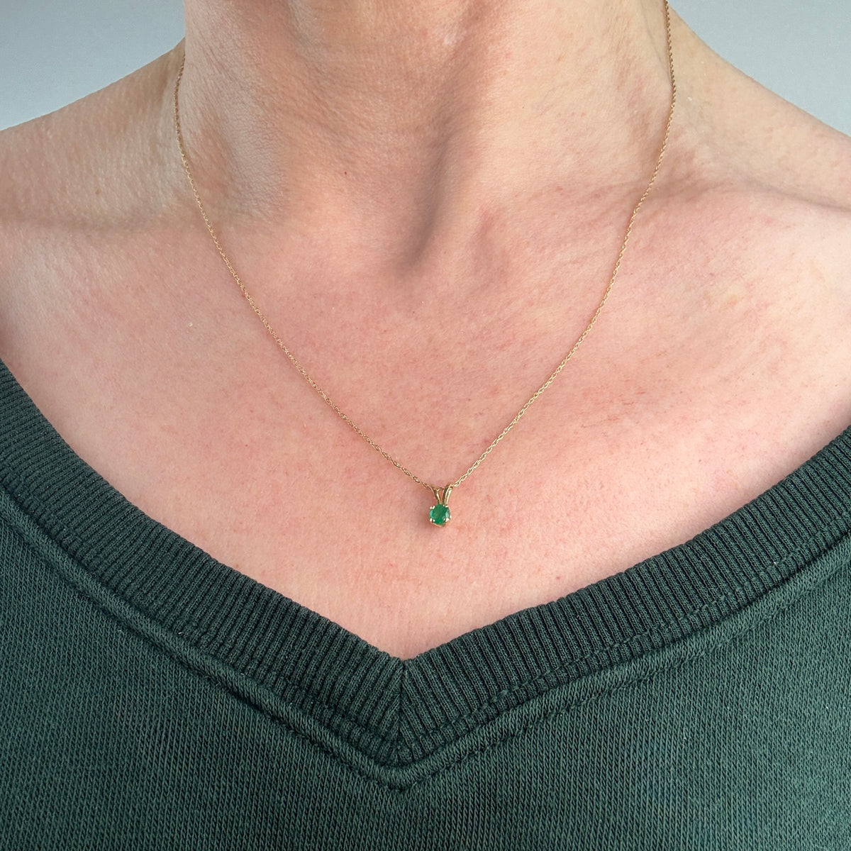 Gold necklace with a green emerald gemstone pendant worn by a person in a dark green sweater.