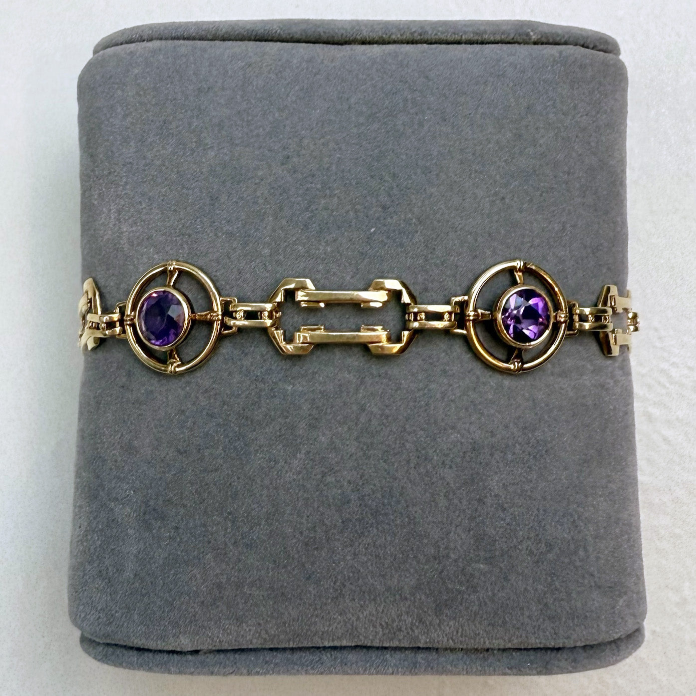 Gold bracelet with purple gemstones on a gray cushion