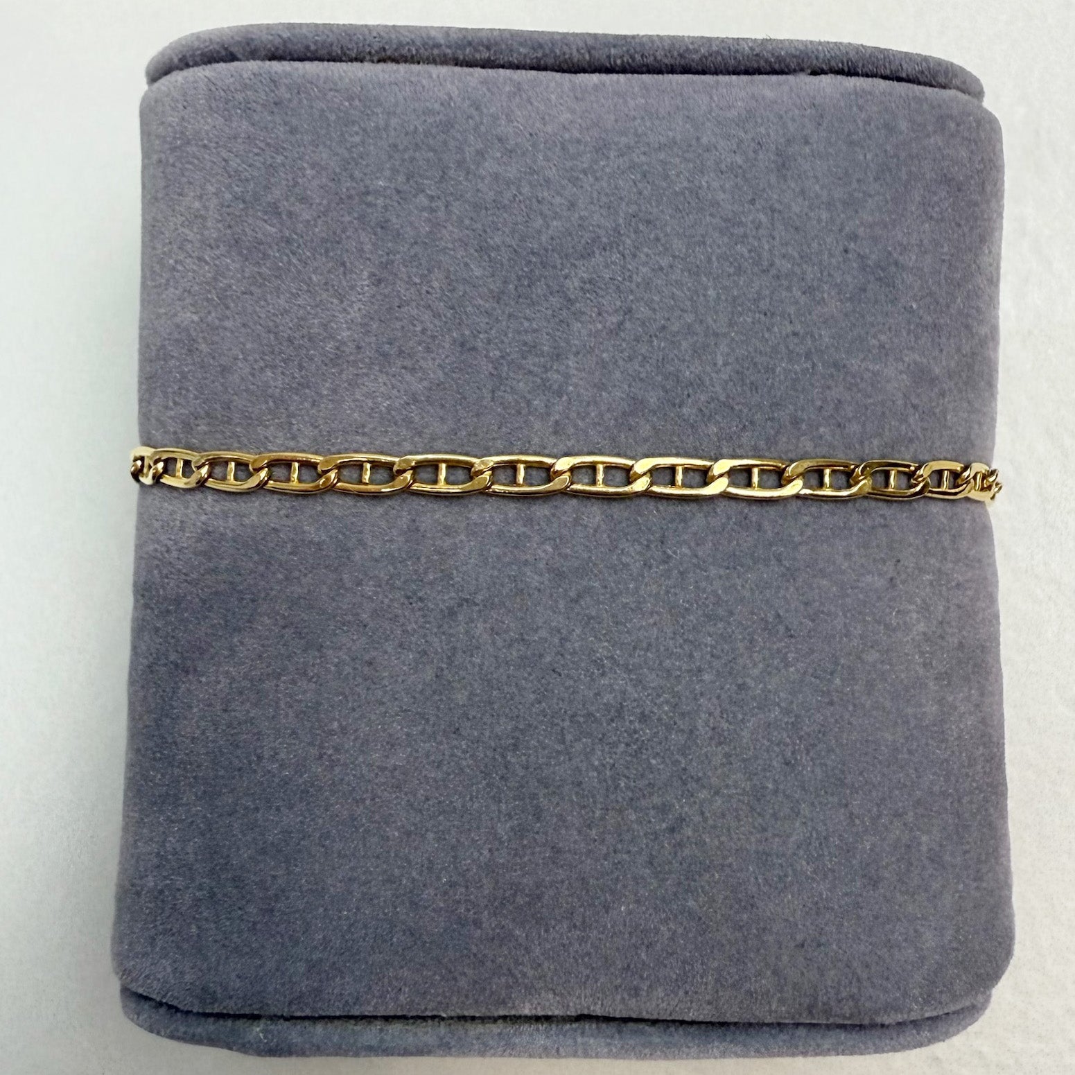 Gold chain bracelet on a gray velvet cushion