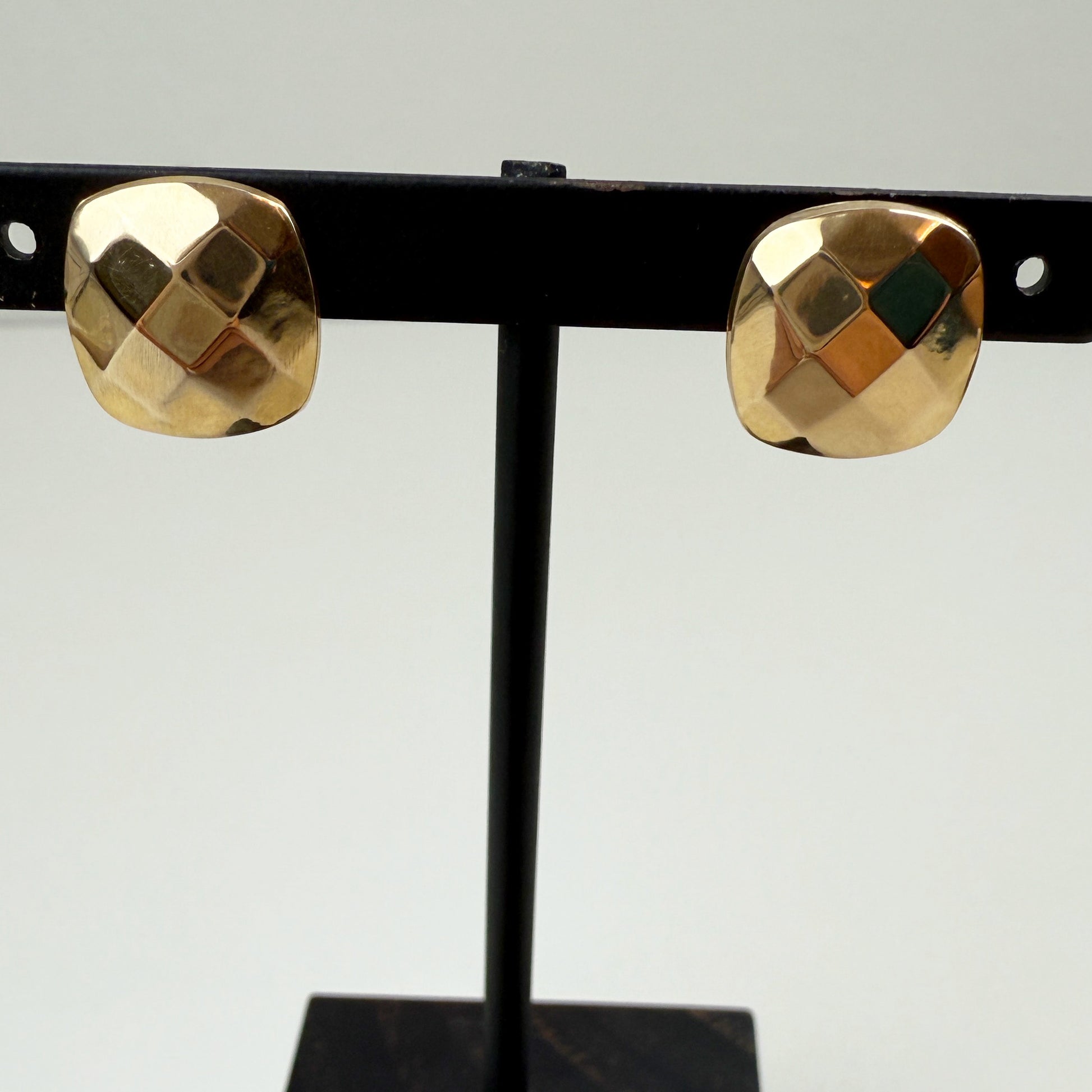 Gold earrings on a black stand against a light gray background