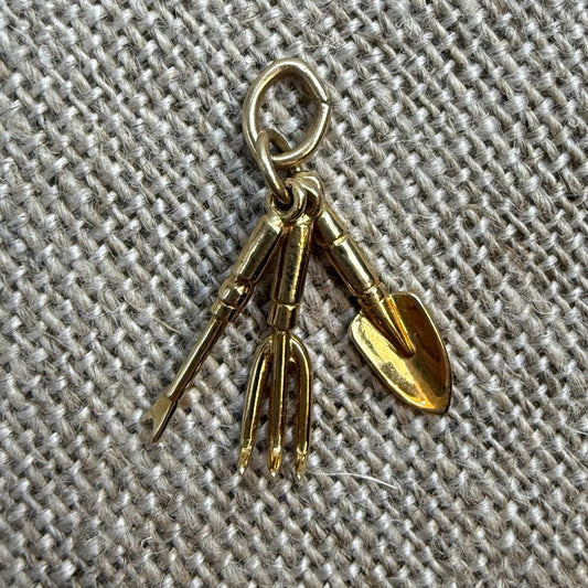 Gold-colored gardening tool charm on a textured fabric background