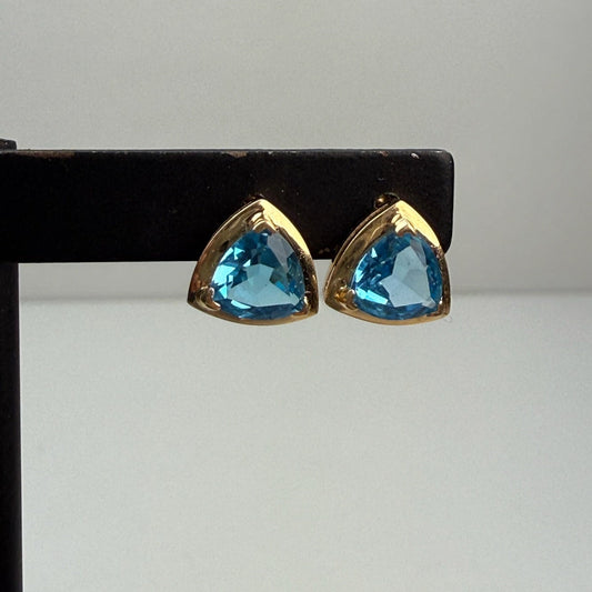 Gold-trimmed blue gemstone earrings on a black stand against a white background