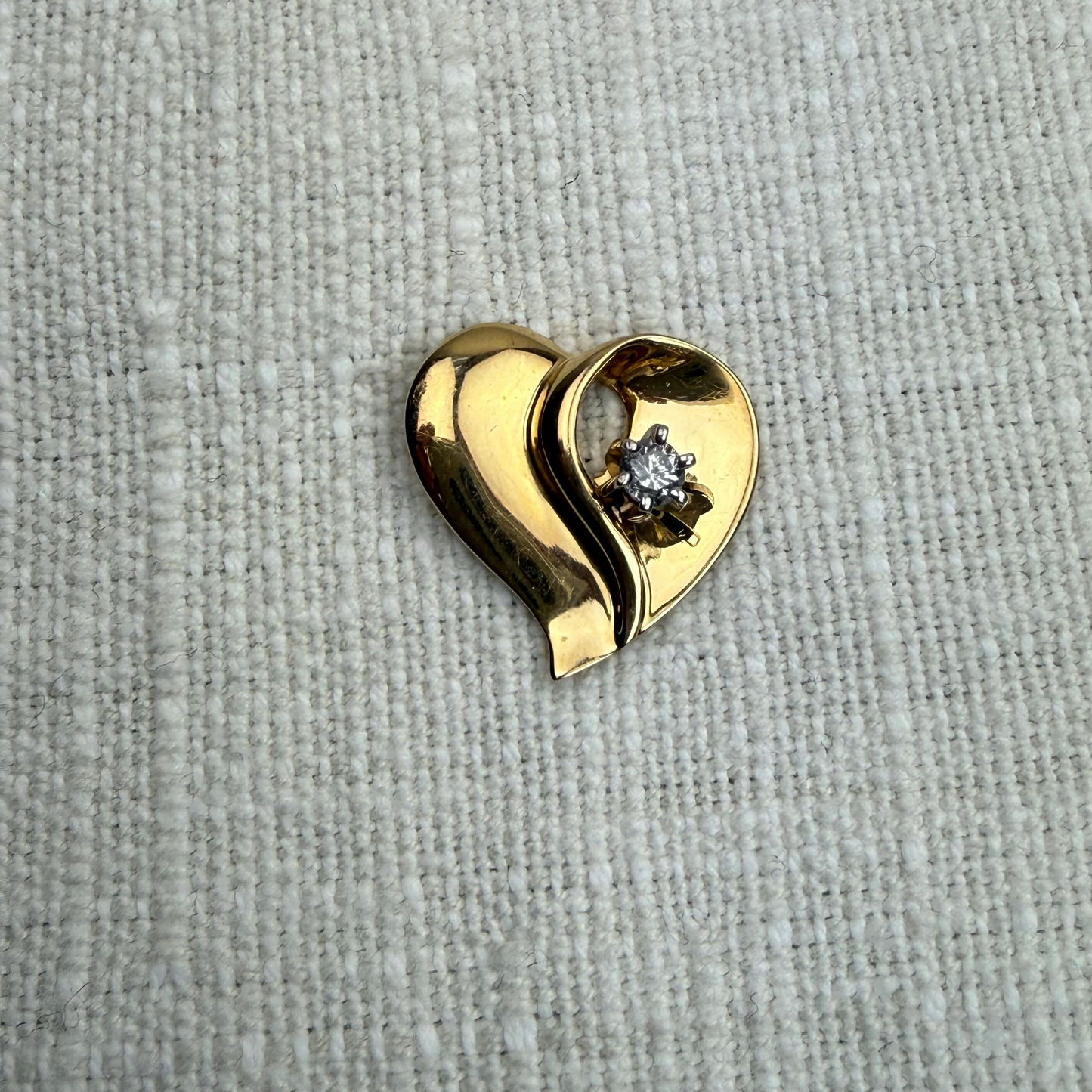 Gold heart-shaped pendant with a diamond on a textured beige background