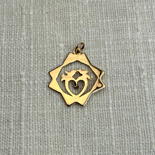 Gold pendant with heart and fish design on a gray fabric background