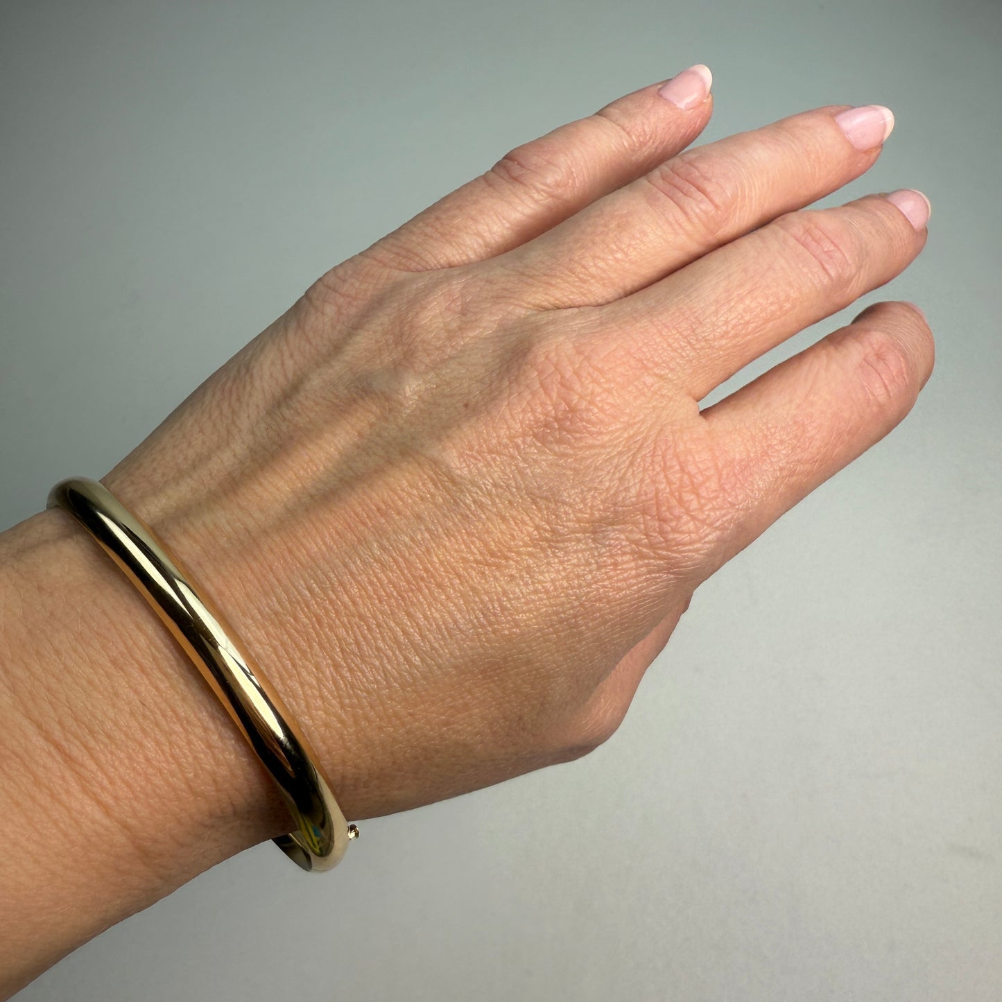 Polished oval gold hinged bangle on a wrist.
