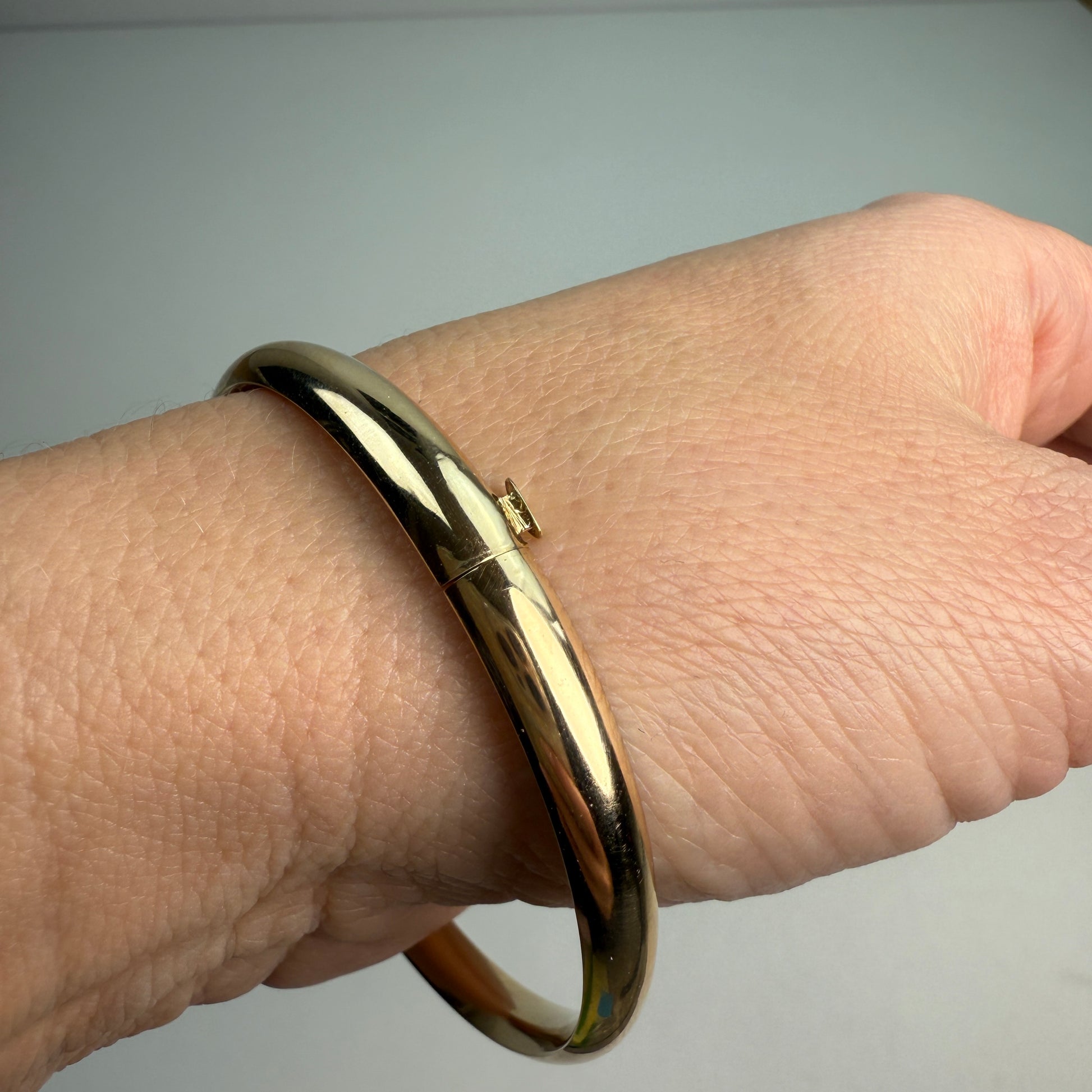 Polished oval gold hinged bangle on a wrist.