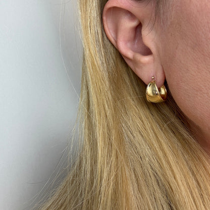 Gold hoop earrings worn by a person with blonde hair against a neutral background