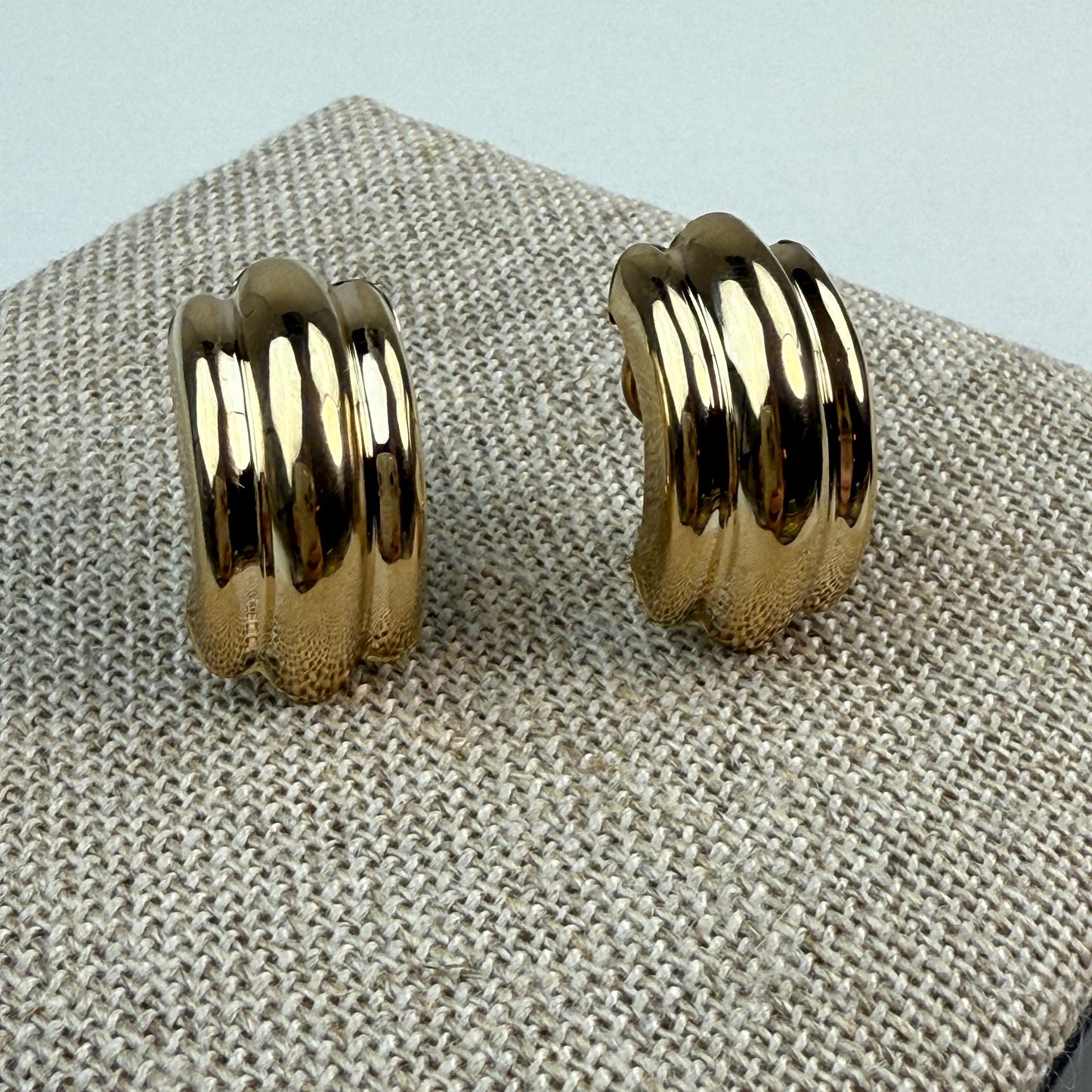 front of ribbed gold earrings on a burlap textured background 