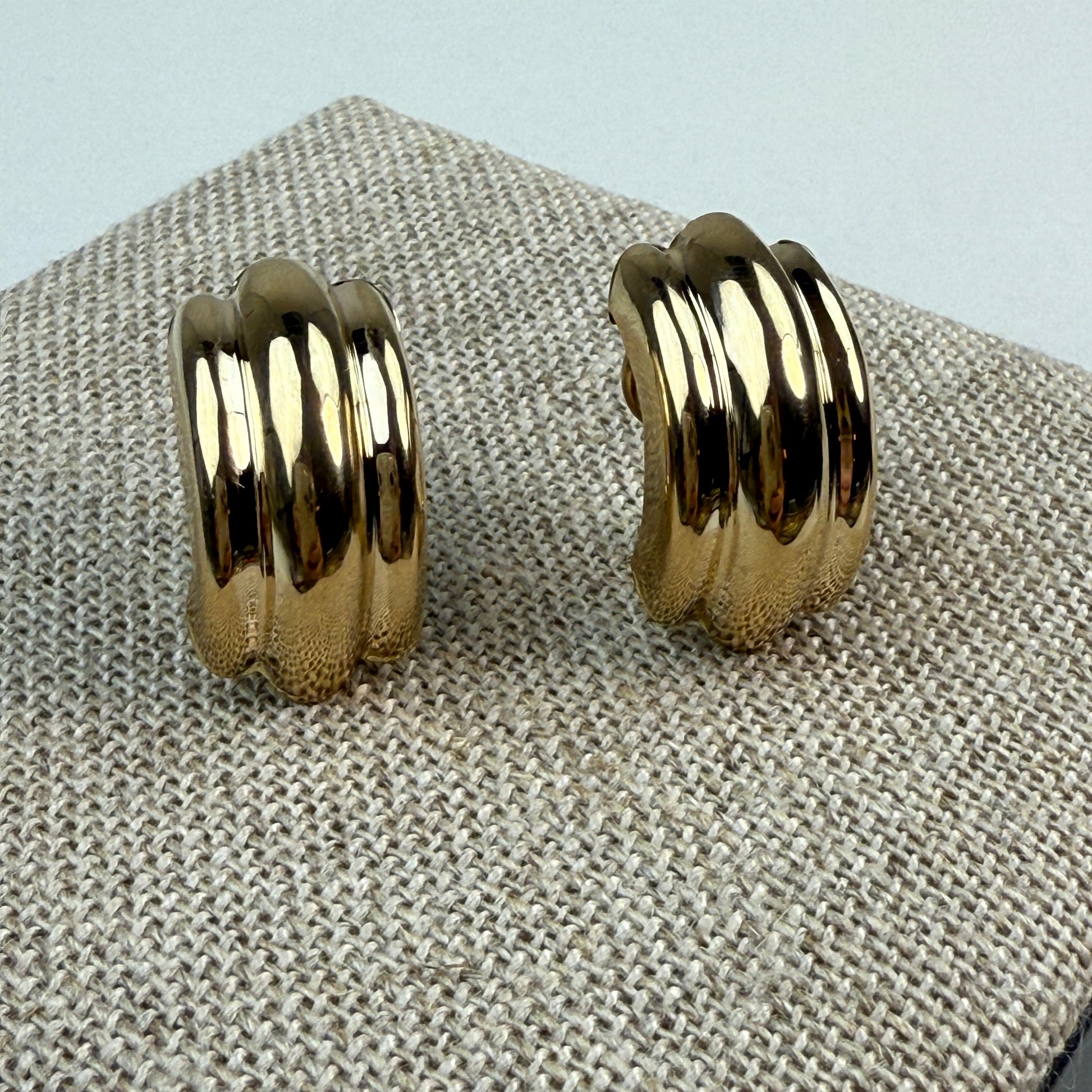 front of ribbed gold earrings on a burlap textured background 