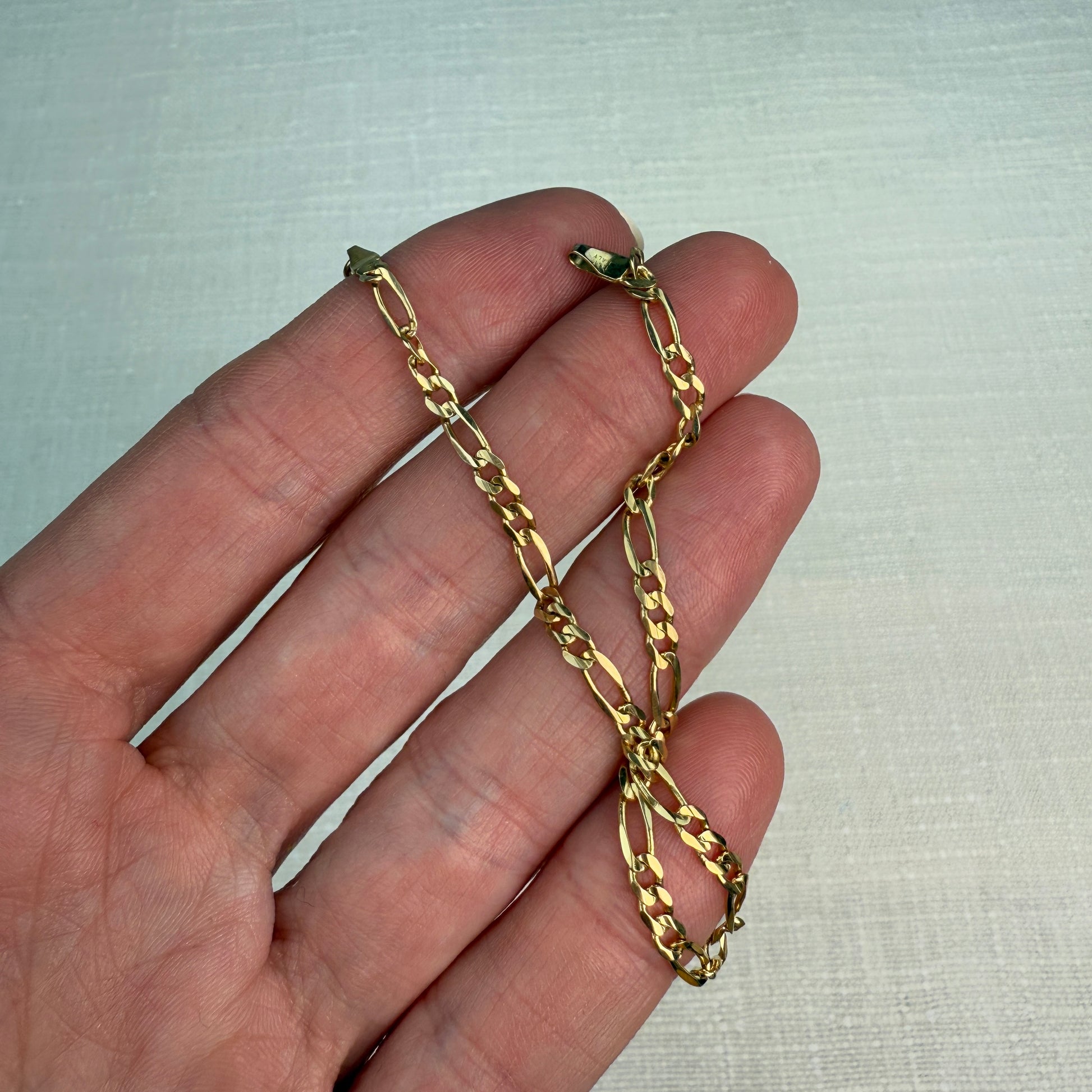 Figaro gold chain shown in a hand. 
