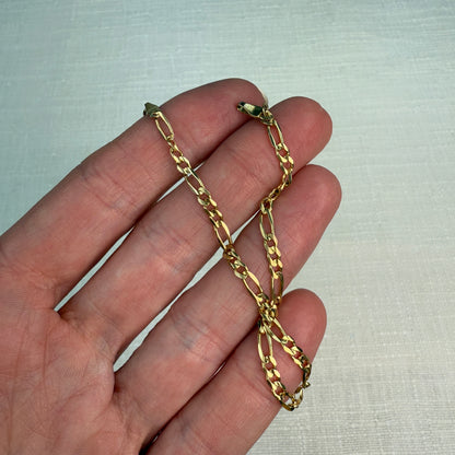 Figaro gold chain shown in a hand. 