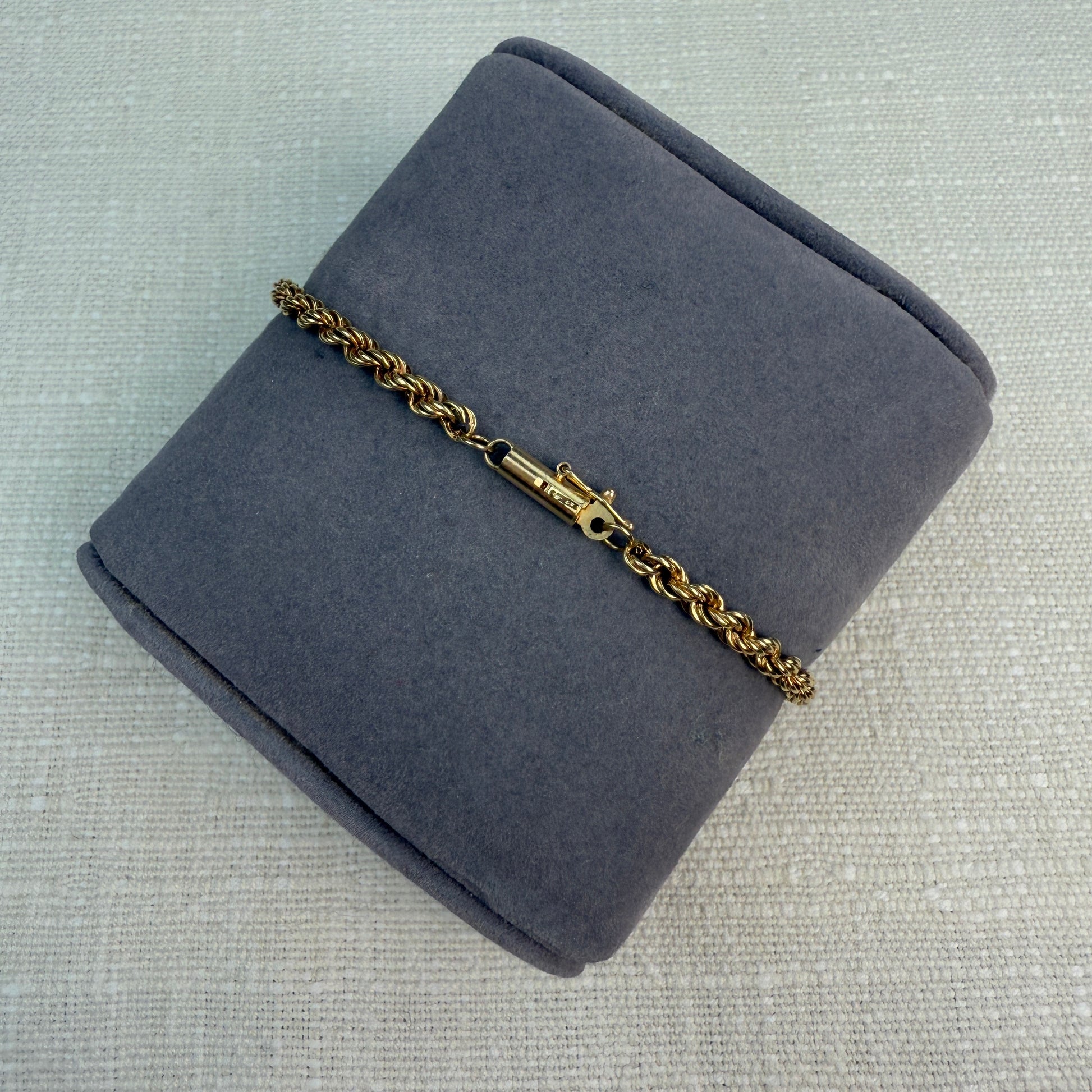 Shiny gold rope chain with a tube clasp shown on grey pillow
