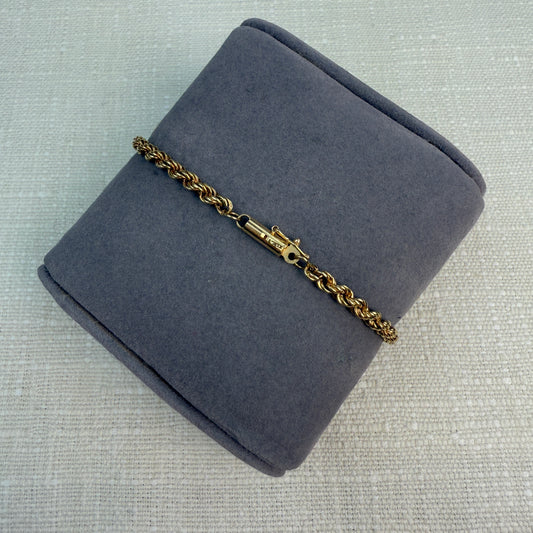 Shiny gold rope chain with a tube clasp shown on grey pillow