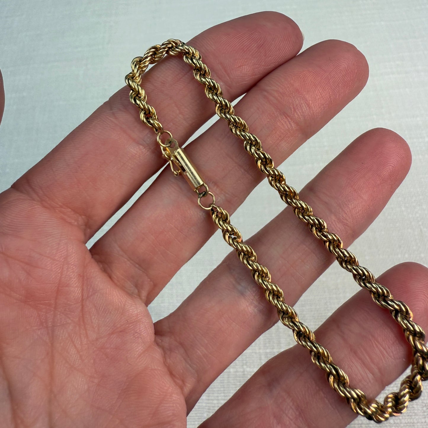 Shiny gold rope chain with a tube clasp shown in hand.