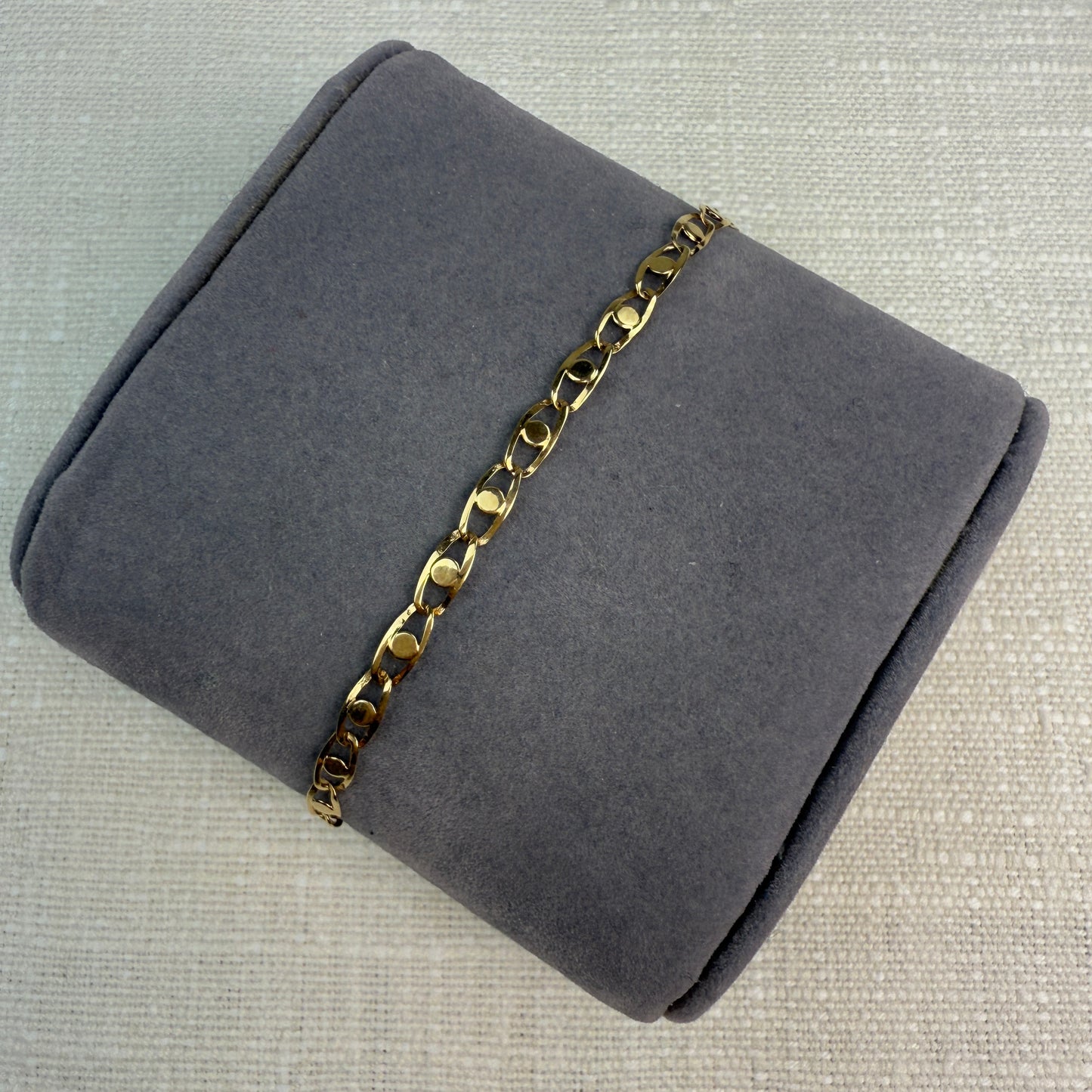 Image of fancy link gold chain on a grey pillow.