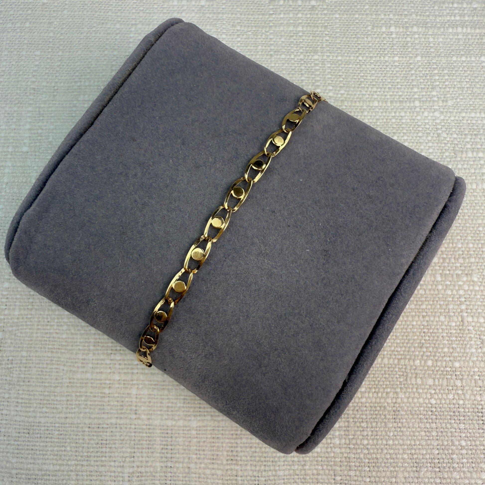 Image of fancy link gold chain on a grey pillow.