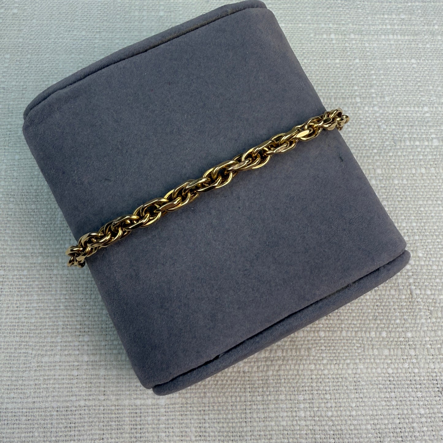 Chunky link gold bracelet shown at an angle on a gray fabric pillow.