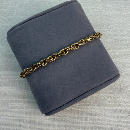 Chunky link gold bracelet shown at an angle on a gray fabric pillow.