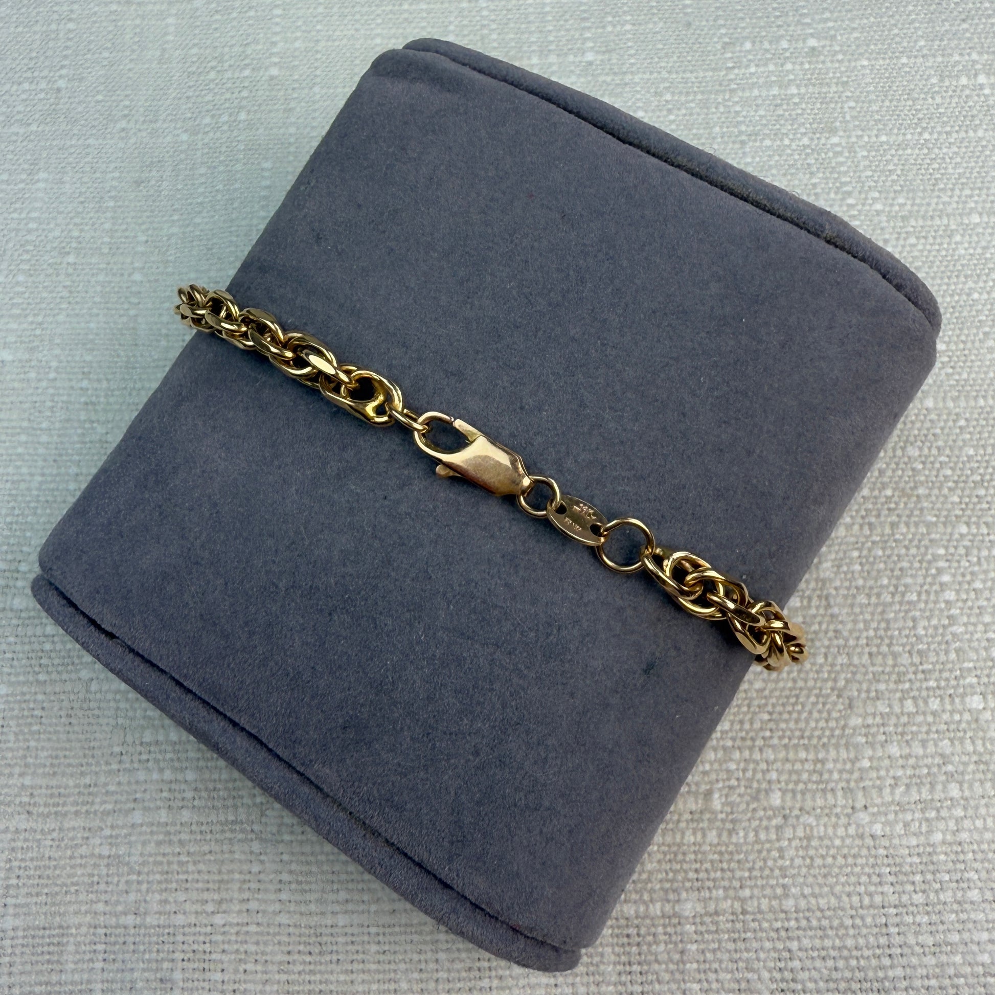 Back view of a chunky gold rope bracelet on a gray fabric pillow, showing the lobster clasp.