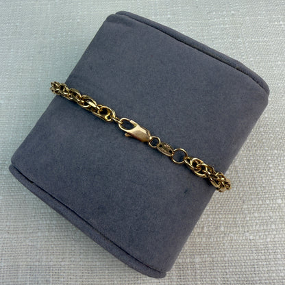 Back view of a chunky gold rope bracelet on a gray fabric pillow, showing the lobster clasp.