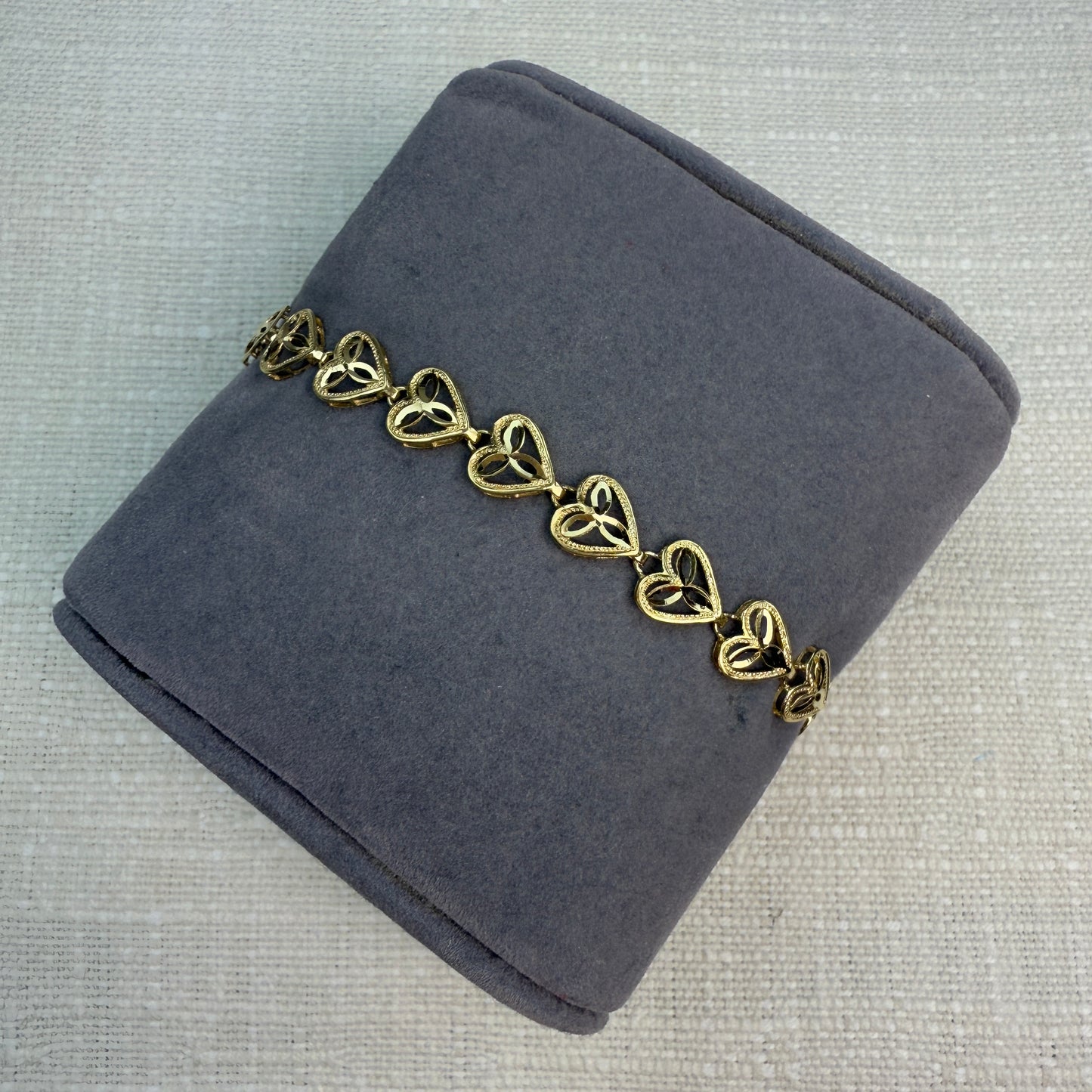 Gold filigree heart bracelet displayed on a gray fabric pillow.