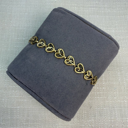 Gold filigree heart bracelet displayed on a gray fabric pillow.