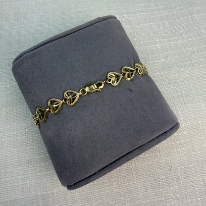 Gold filigree heart bracelet displayed on a gray fabric pillow, highlighting a lobster clasp.
