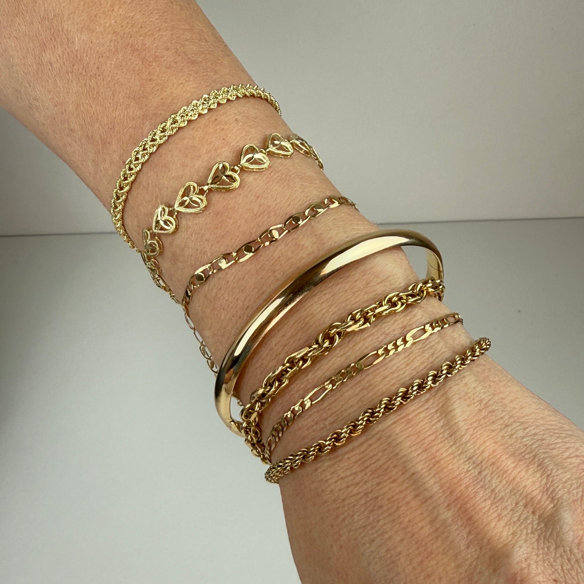 Seven yellow gold bracelets stacked on a woman’s wrist, showing scale and layering.
