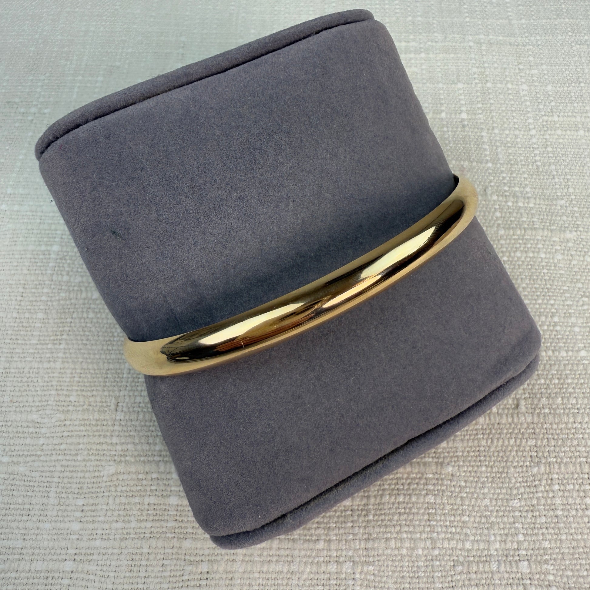 Polished oval gold hinged bangle on a grey pillow.