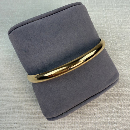Polished oval gold hinged bangle on a grey pillow.