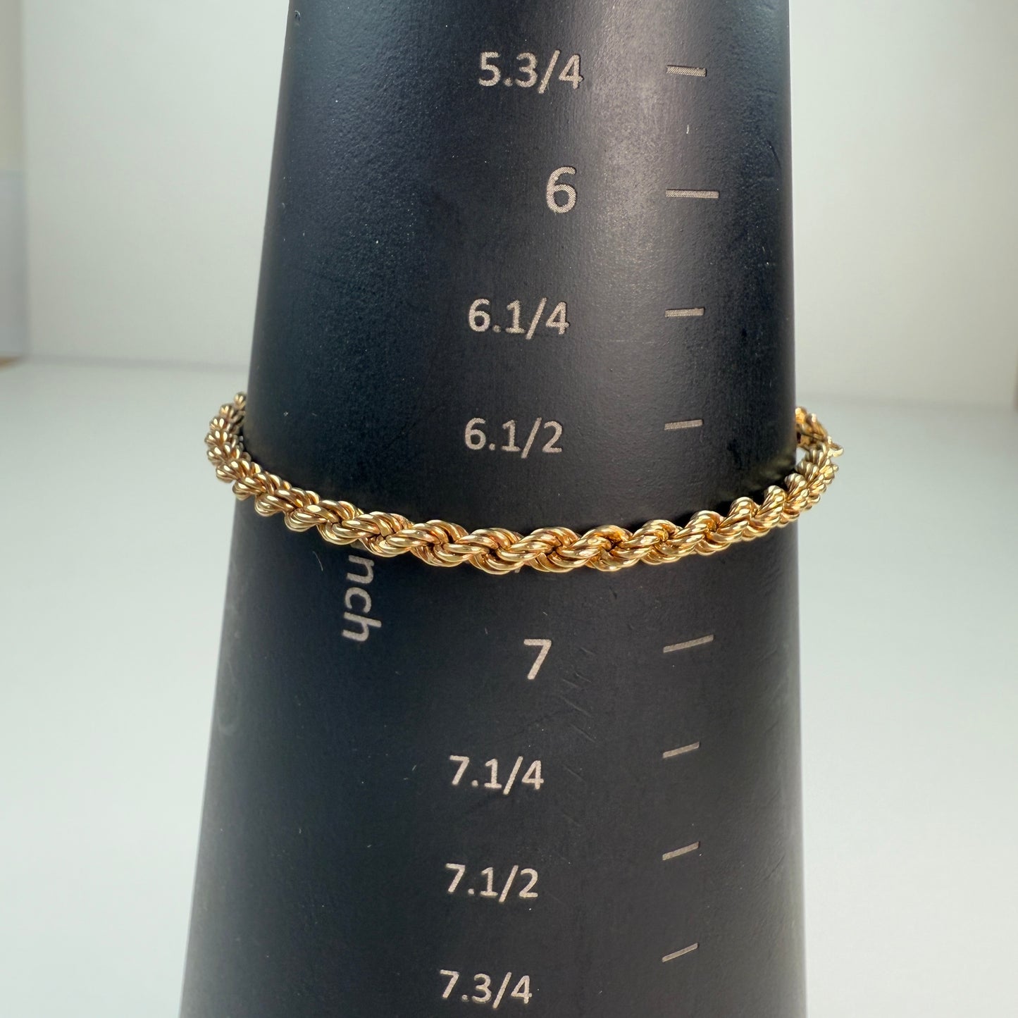 Shiny gold rope chain displayed on a black mandrel with white inch markings, measuring 6.75 inches.