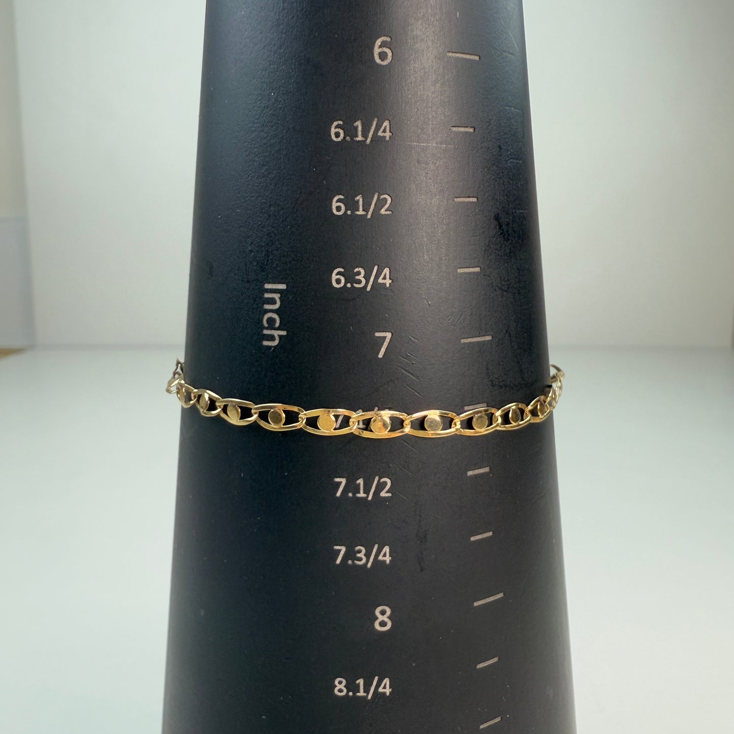 Shiny gold fancy link bracelet displayed on a black mandrel with white inch markings, measuring 7.25 inches.