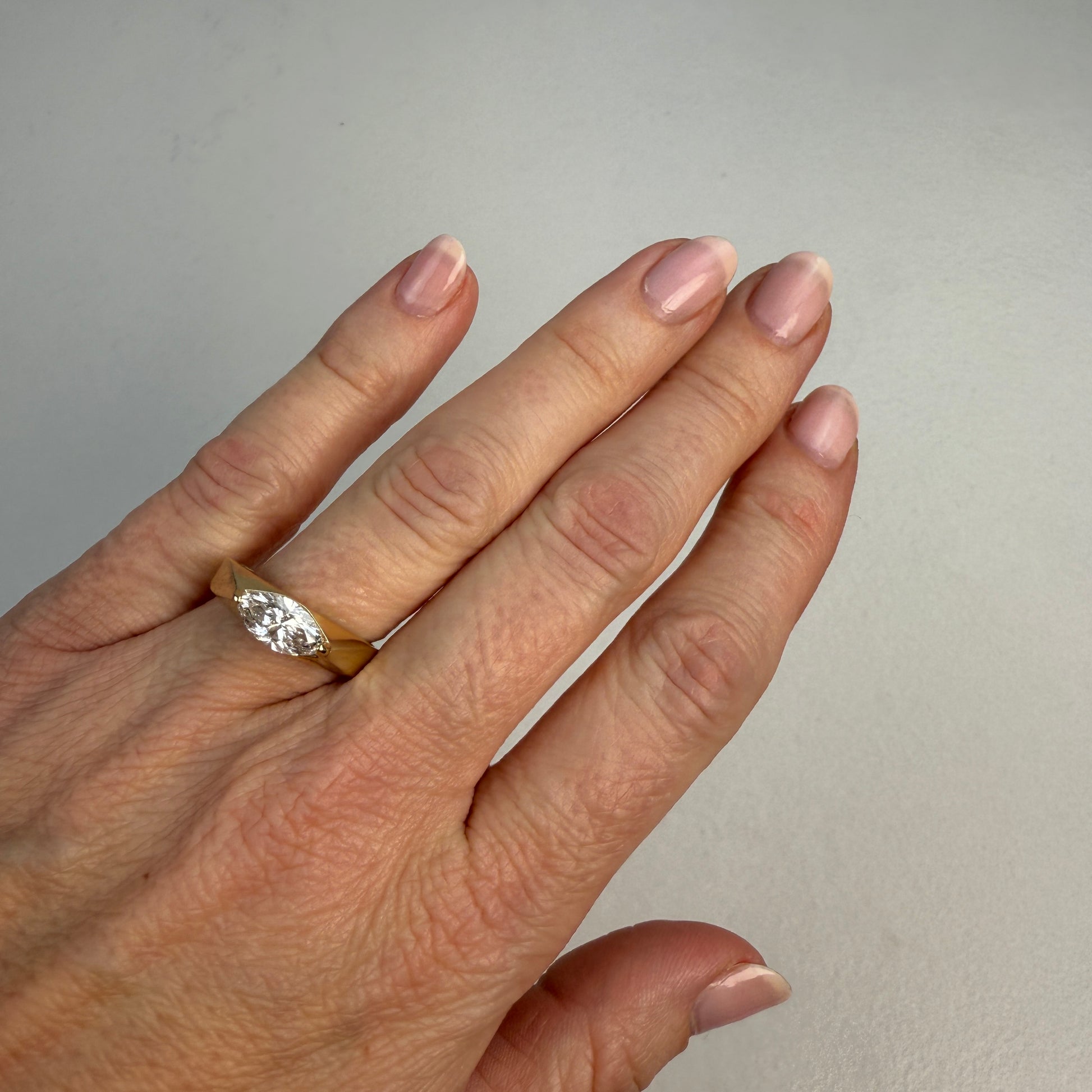 Hand wearing a gold ring with a diamond on a plain background
