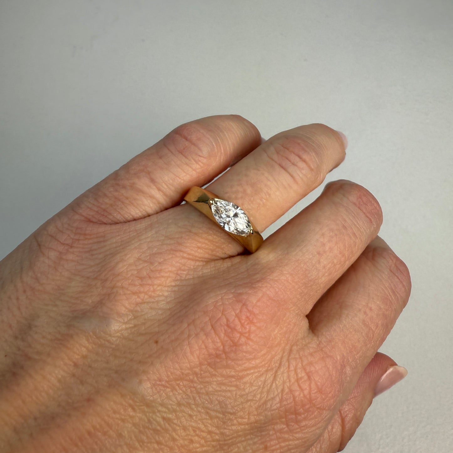 Hand wearing a gold ring with a diamond on a neutral background