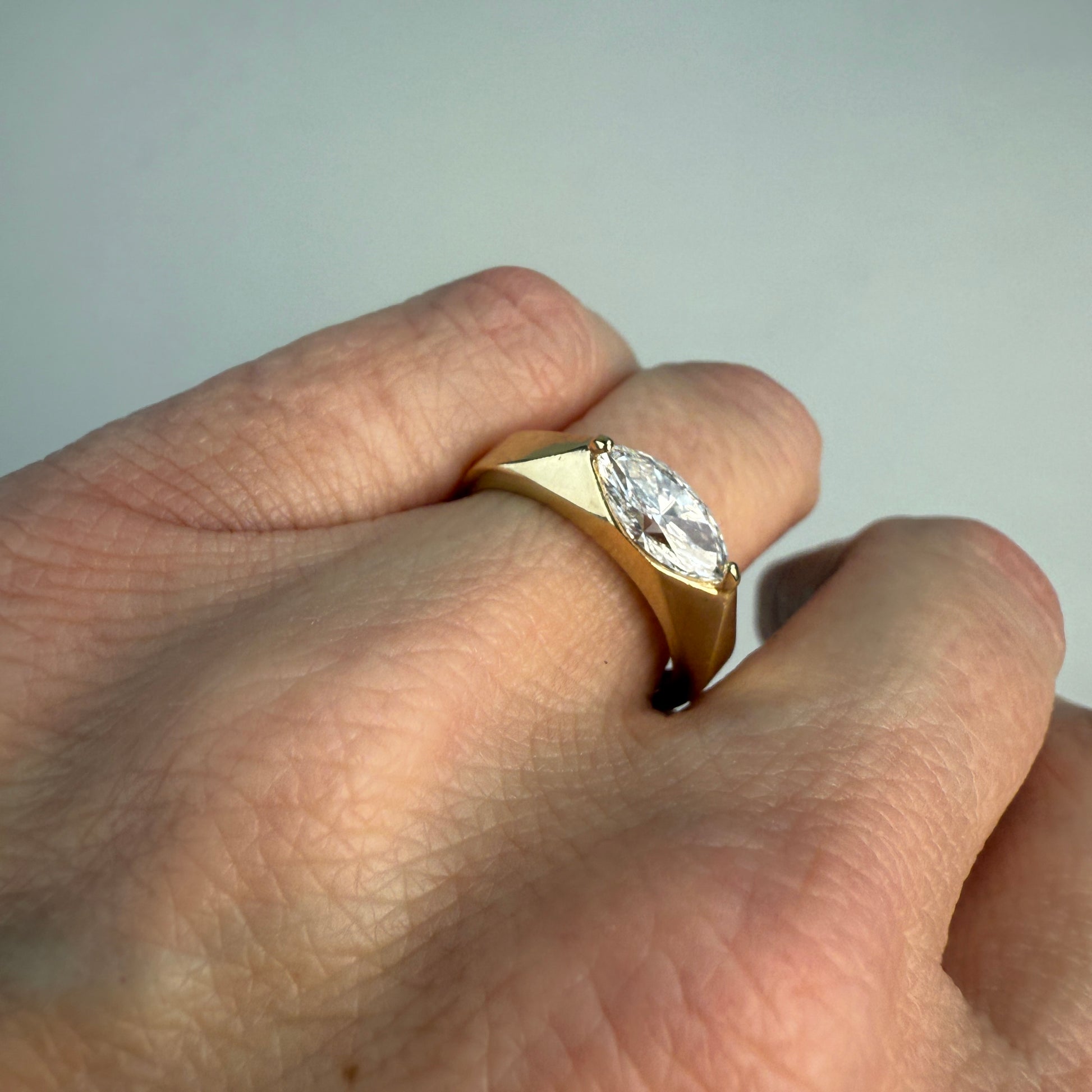 Gold ring with a diamond on a finger against a neutral background