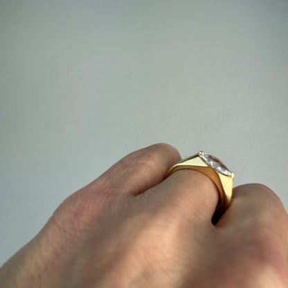 Gold ring with a diamond on a finger against a plain background