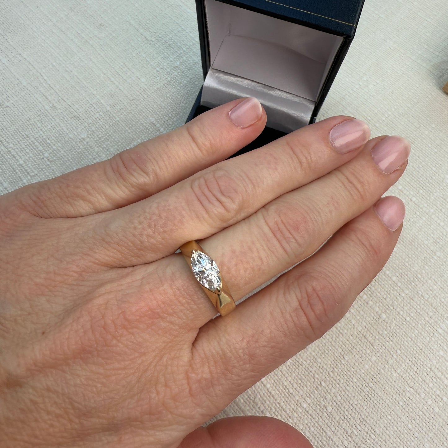 Hand wearing a diamond ring with an open jewelry box in the background