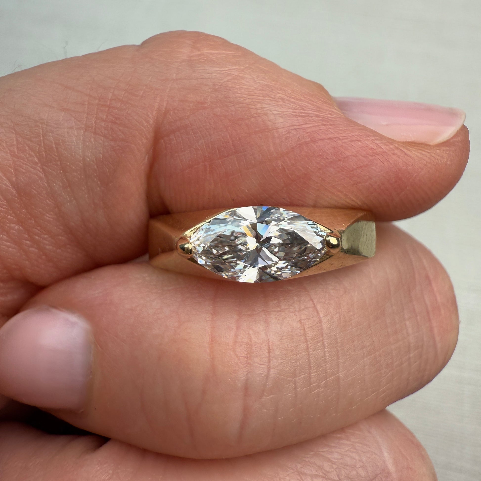 Gold ring with a large diamond held between fingers against a neutral background
