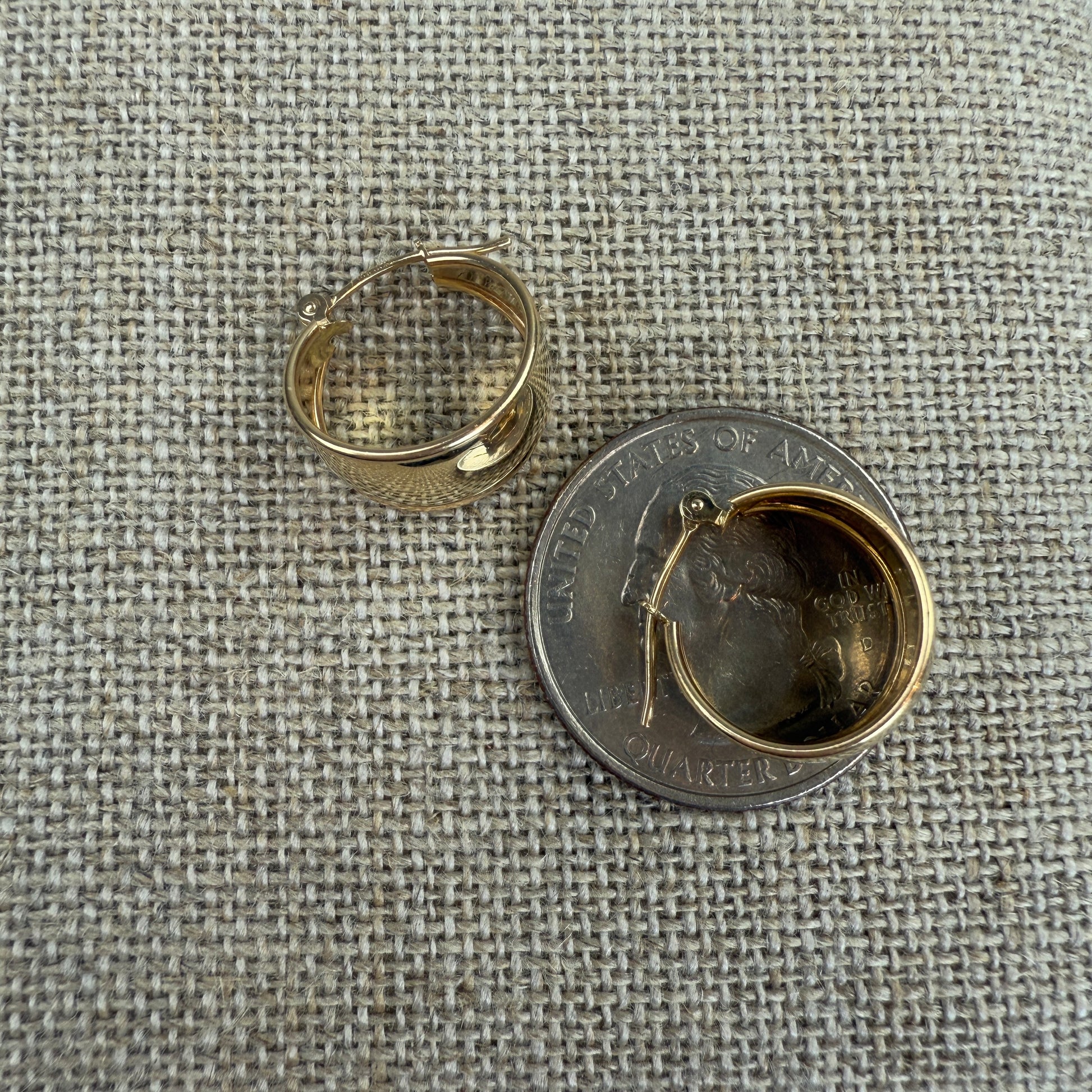 Gold hoop earring next to a quarter on a textured fabric background