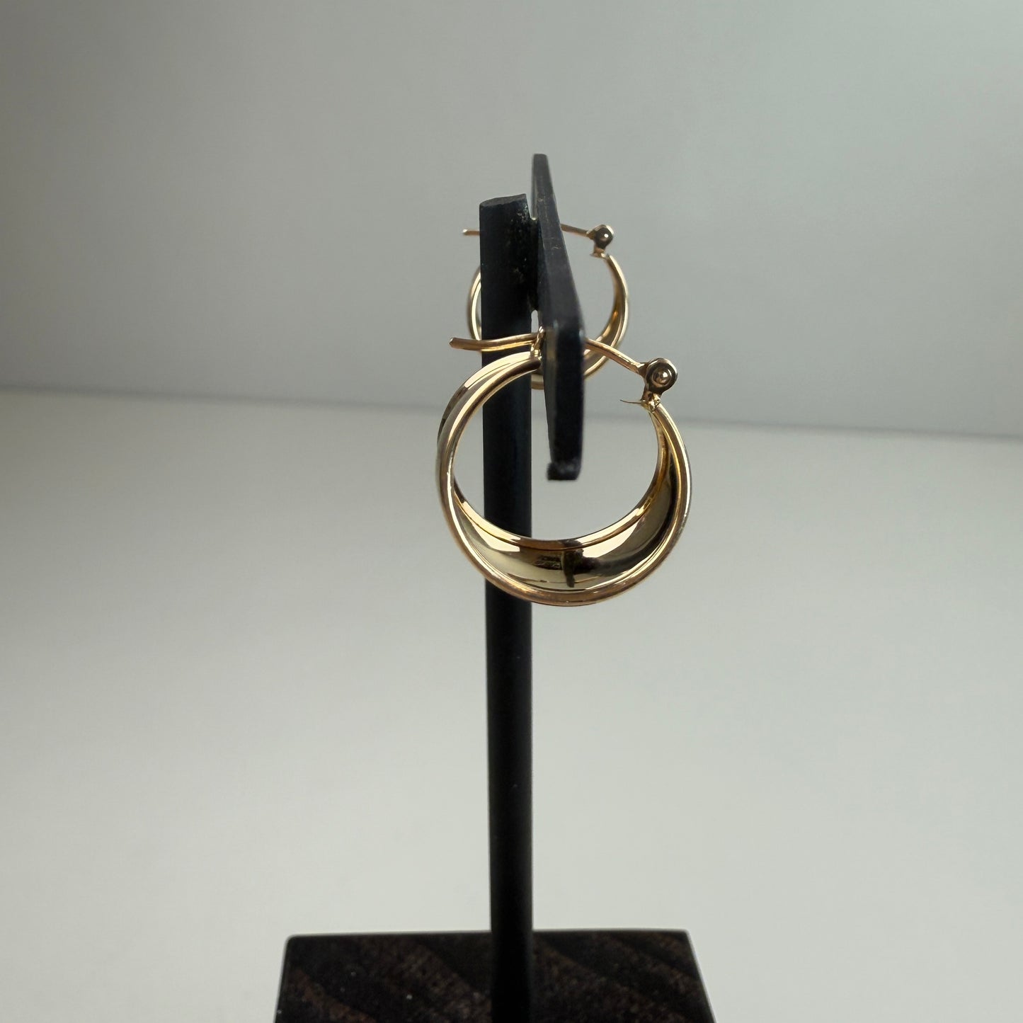 Gold hoop earrings on a black stand against a gray background