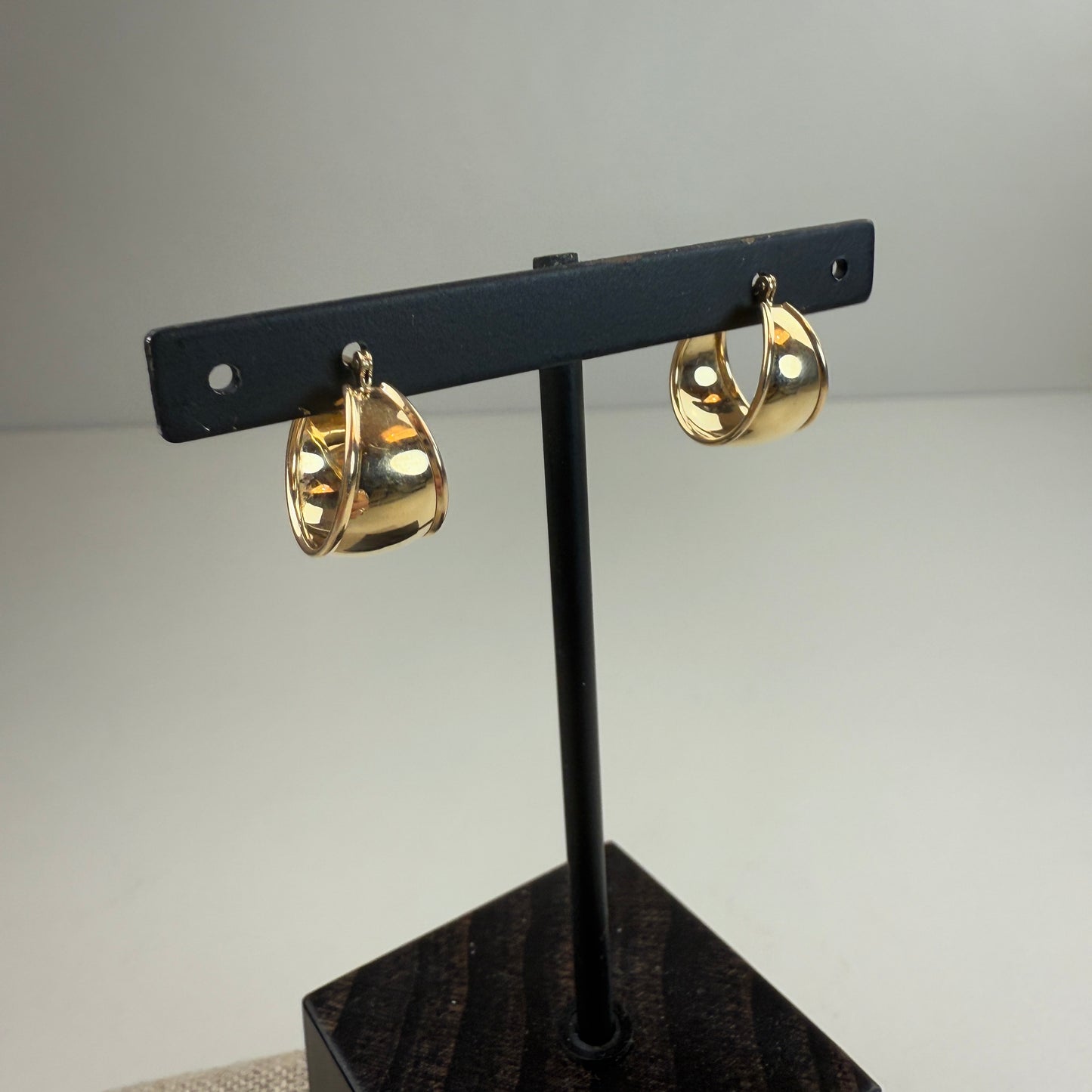 Gold hoop earrings on a black stand against a gray background