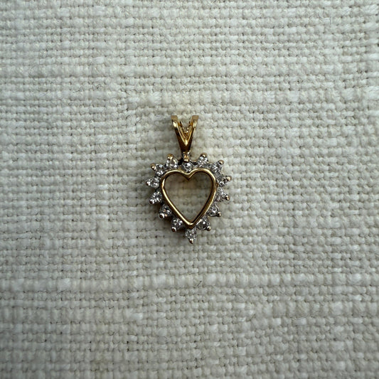 Gold heart-shaped pendant with a diamond-like stone on a textured gray background