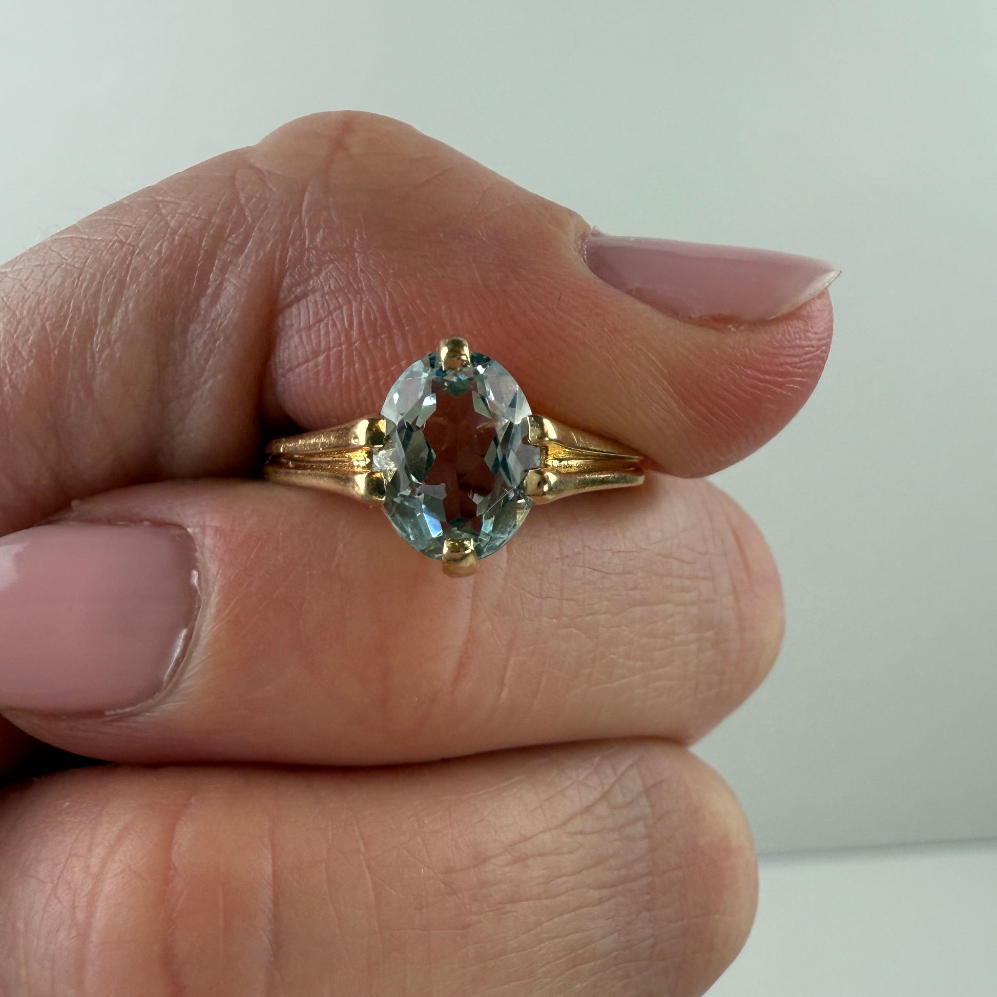 Gold ring with an aquamarine gemstone held on a finger against a plain background
