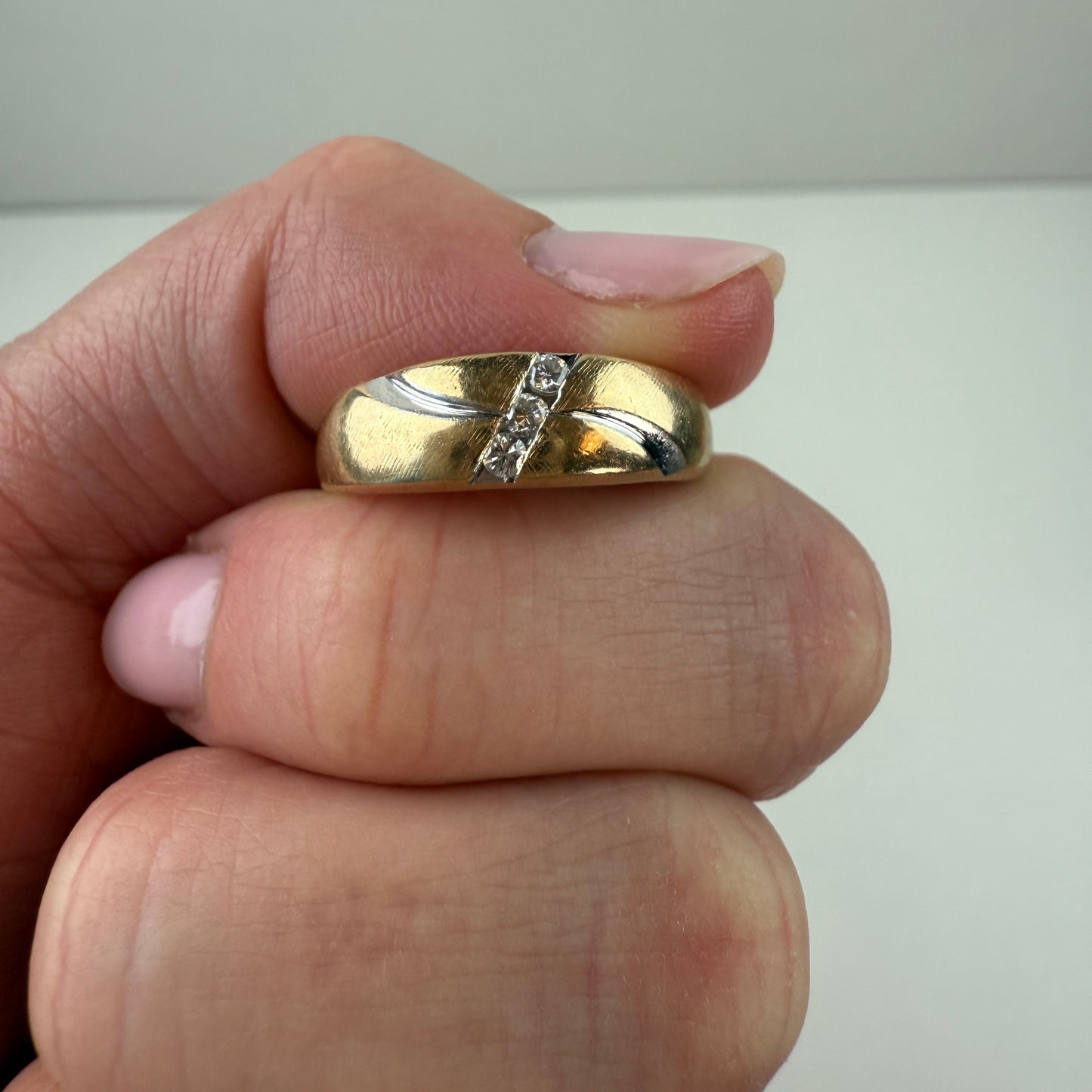 Gold ring with a diamond on a finger against a neutral background