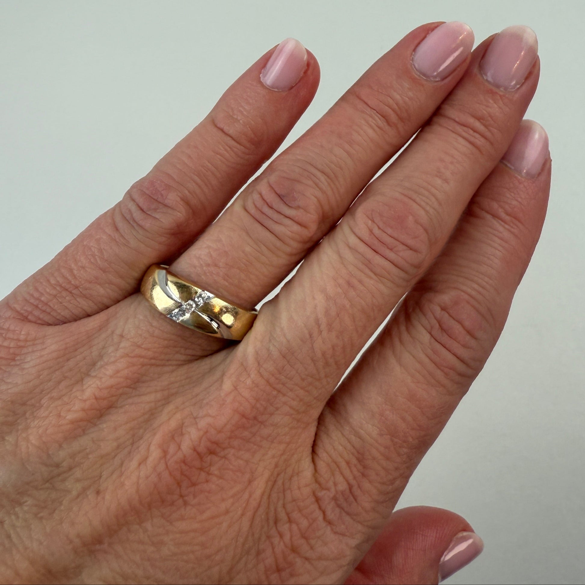Hand wearing a gold ring with a white stone on a plain background