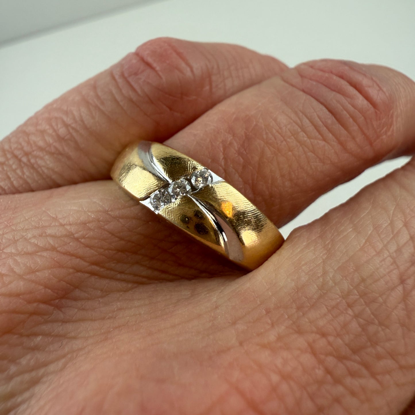 Gold ring with diamonds on a finger against a white background