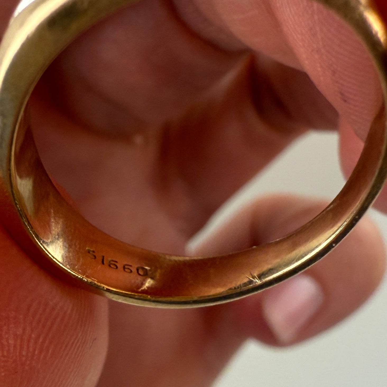 Gold ring held between fingers against a neutral background